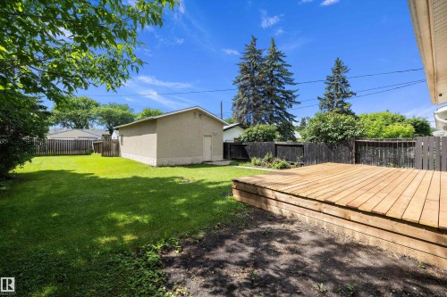 Expansive backyard featuring a large wooden deck, manicured lawn, and a detached structure with an exterior door - 12912 103 Street, Edmonton, AB 