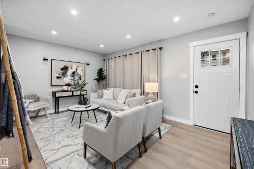 Bright living area featuring wood-finish flooring, recessed lighting, and a white paneled entry door with windowpanes - 12912 103 Street, Edmonton, AB 