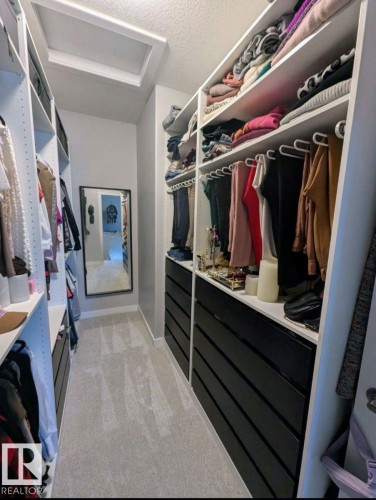 Walk-in closet featuring custom built-in shelving, integrated hanging rods, black drawer units, light-toned carpeting, and a wall-mounted mirror - 2327 Frezenberg Avenue, Edmonton, AB 