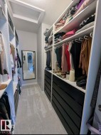 Walk-in closet featuring custom built-in shelving, integrated hanging rods, black drawer units, light-toned carpeting, and a wall-mounted mirror - 