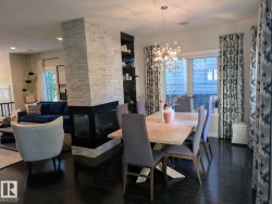 Open-concept dining area featuring dark wood-finish flooring, a modern chandelier, and a two-sided stone-clad fireplace - 