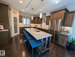 Gourmet kitchen featuring a large central island with seating, dark wood-finish flooring, white tile backsplash, stainless steel appliances, and abundant cabinetry - 
