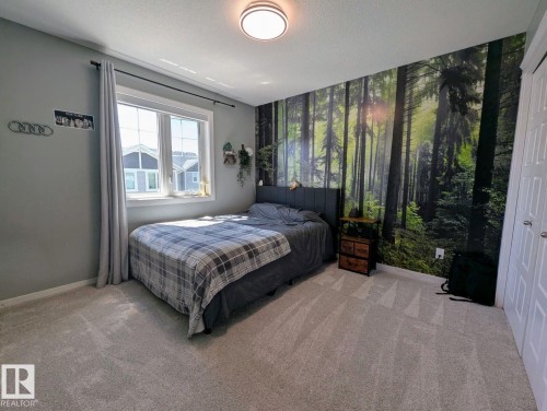 Carpeted room featuring a large window with white sills and trim, light gray walls, a full wall mural depicting a forest scene, and white bifold closet doors - 2327 Frezenberg Avenue, Edmonton, AB 