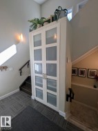 Entryway featuring gray patterned tile flooring, a built-in storage unit with frosted glass panel doors, and a wood staircase with dark risers and treads - 