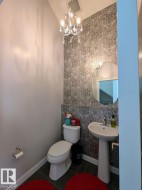 Powder room featuring a pedestal sink, white toilet, and dark tile flooring - 