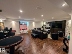 Spacious lower-level living area featuring wood-finish flooring, recessed lighting, and a contemporary linear fireplace - 