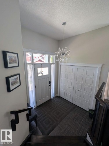 Bright entryway featuring a contemporary crystal chandelier, white panel door with glass sidelights and transom, dark patterned floor tiles, and bi-fold closet doors - 2327 Frezenberg Avenue, Edmonton, AB 