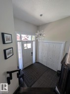 Bright entryway featuring a contemporary crystal chandelier, white panel door with glass sidelights and transom, dark patterned floor tiles, and bi-fold closet doors - 