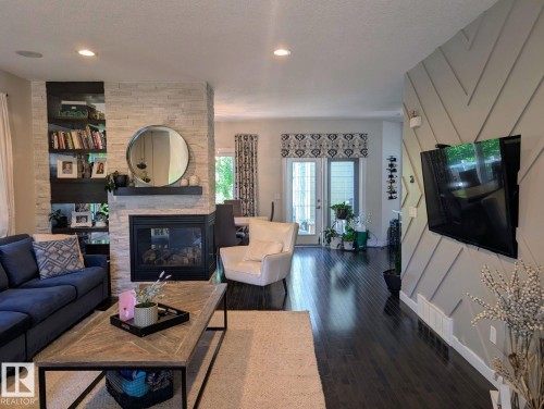 Living area featuring a gas fireplace with stacked stone surround, built-in shelving, dark wood-finish flooring, and French doors - 2327 Frezenberg Avenue, Edmonton, AB 