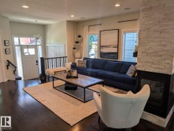Open-concept living area featuring rich wood-finish flooring, a contemporary stone-clad fireplace, and recessed lighting - 