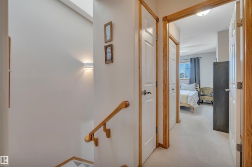 Upper-level hallway featuring light wood-finish trim, white paneled doors, and neutral carpeting - 207-4807 43A Ave, Leduc, AB 