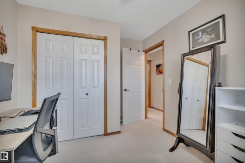 Interior room featuring a neutral color palette, wood-trim doorways, white bi-fold closet doors, and light-toned carpeting - 207-4807 43A Ave, Leduc, AB 