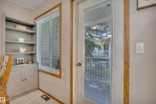 Window with blinds, and white paneled door with integrated blinds, all framed by wood trim - 207-4807 43A Ave, Leduc, AB 