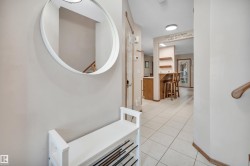 Entryway featuring a large circular mirror, light neutral wall paint, and tile flooring - 