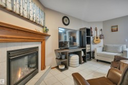 Living area featuring a fireplace with a wood mantle and tile surround, accompanied by neutral tile flooring - 