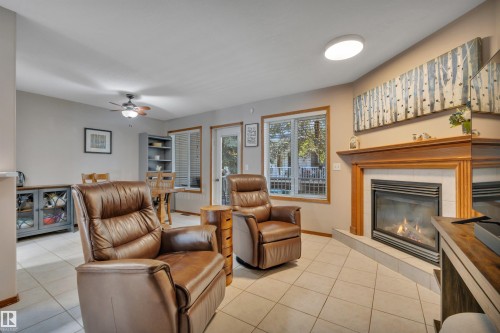 Living area featuring tile flooring, a fireplace with a wood mantel and tile surround, and a ceiling fan - 207-4807 43A Ave, Leduc, AB 