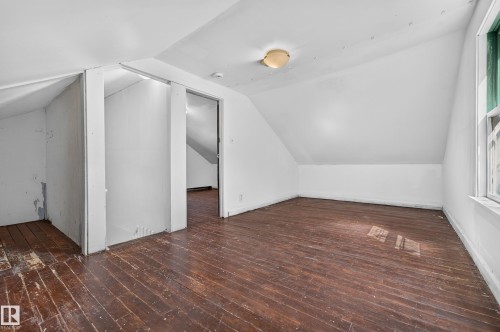 Room featuring wood-finish flooring, sloped ceilings, and a window with green trim - 11708 79 Street, Edmonton, AB 