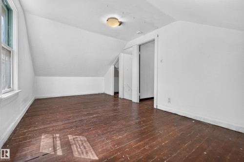 Attic space featuring sloped ceilings, a single-pane window, wood-finish flooring, and a flush-mount ceiling light - 11708 79 Street, Edmonton, AB 