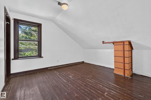 Attic space featuring an angled ceiling, dark-stained wood-finish flooring, and a single-pane window with dark trim - 11708 79 Street, Edmonton, AB 