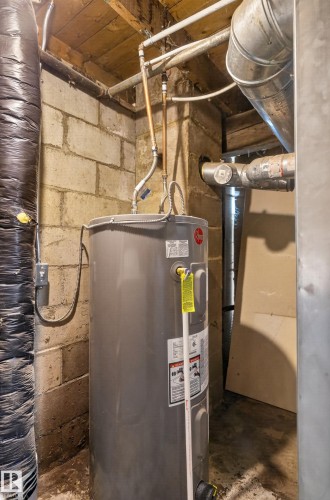 Gray water heater unit with associated copper and galvanized piping, set against a concrete block wall - 11708 79 Street, Edmonton, AB 