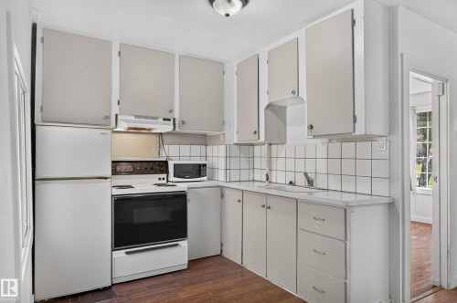 Compact kitchen featuring white cabinetry, a built-in oven with cooktop, a white refrigerator, and a microwave - 11708 79 Street, Edmonton, AB 