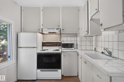Galley kitchen featuring white cabinetry, tile countertops, a white top-mount sink, and a window - 11708 79 Street, Edmonton, AB 