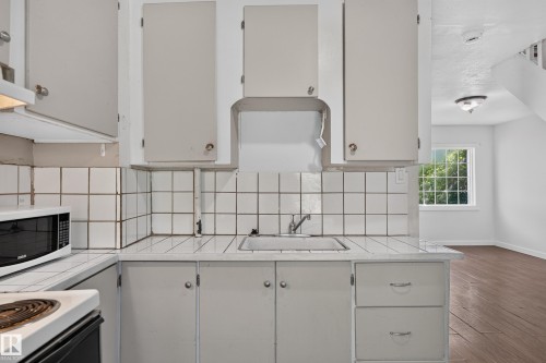 Kitchen area featuring white cabinetry, a built-in sink, and square tile countertops with a matching backsplash - 11708 79 Street, Edmonton, AB 