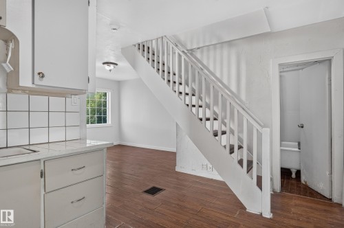 White painted staircase with wood-finish treads, leading from a room featuring wood-finish flooring and a white tile backsplash - 11708 79 Street, Edmonton, AB 
