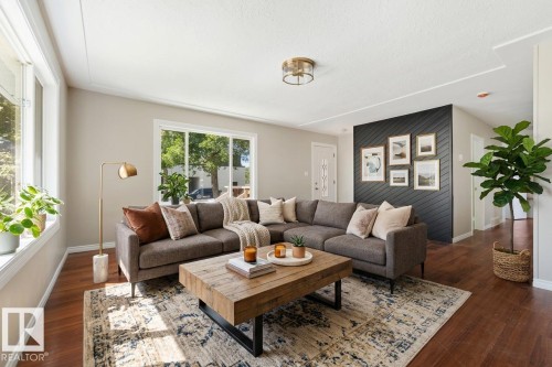 The virtual staging emphasizes the room's excellent flow and spaciousness while making it feel warm and move-in ready. The layout draws the eye naturally from the bright windows and feature wall allowing a buyer to envision this space - 10602 100 Avenue, Fort Saskatchewan, AB - Indoor Photo Showing Living Room