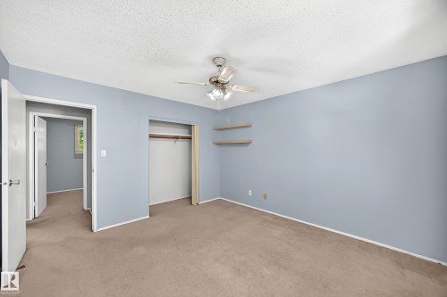 Bedroom featuring light blue walls, brown carpet, a ceiling fan, an open closet with a hanging rod, and two wall-mounted shelves - 355 Northgate Terrace, Edmonton, AB 
