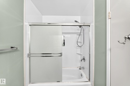 Bathtub with sliding glass enclosure featuring a chrome frame, integrated shelving, and a handheld showerhead - 355 Northgate Terrace, Edmonton, AB 