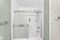 Bathtub with sliding glass enclosure featuring a chrome frame, integrated shelving, and a handheld showerhead - 
