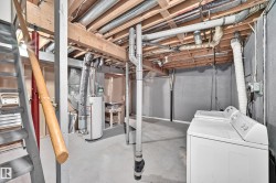Unfinished basement featuring exposed wood joists, concrete flooring, and an accessible water heater - 