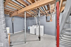 Utility area featuring a concrete floor, painted block walls, exposed ceiling joists, laundry hookups, and a utility sink - 