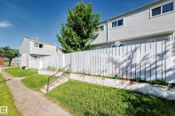 Grey vinyl-sided townhome featuring a white privacy fence, concrete pathway, and mature trees - 
