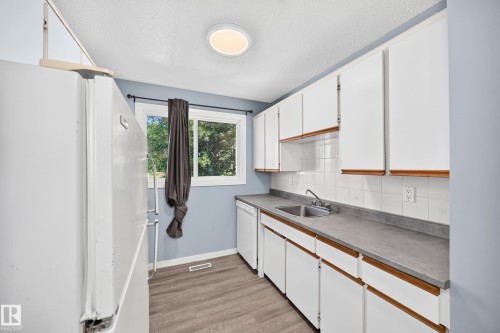 Galley-style kitchen featuring white cabinetry with wood trim, a double basin stainless steel sink, and gray countertops - 355 Northgate Terrace, Edmonton, AB 