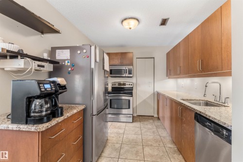 Galley kitchen featuring wood-finish cabinetry, granite-style countertops, and stainless steel appliances - 2324 151 Avenue Nw, Edmonton, AB 