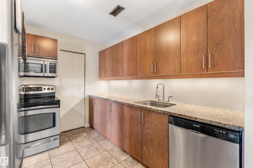 Kitchen featuring wood-finish cabinetry, light-toned countertops, stainless steel appliances, and tile flooring - 2324 151 Avenue Nw, Edmonton, AB 