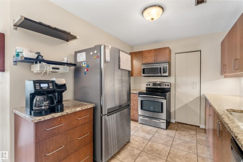 Kitchen featuring tiled flooring, stainless steel appliances, wood-finish cabinetry, and granite-look countertops - 2324 151 Avenue Nw, Edmonton, AB 