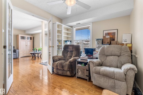 Hardwood flooring extending throughout the room and into the adjacent space, featuring French doors, a ceiling fan with light fixture, built-in shelving, and a large window - 2324 151 Avenue Nw, Edmonton, AB 
