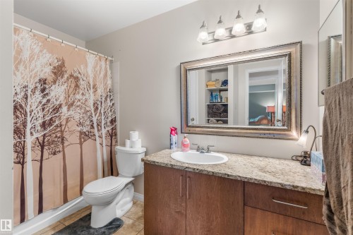 Bathroom featuring a wood-finish vanity with an integrated sink, a speckled countertop, and a framed mirror - 2324 151 Avenue Nw, Edmonton, AB 