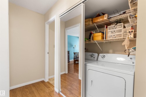 Laundry closet with a stackable washer and dryer, wire shelving, wood-finish flooring, and a mirrored closet door - 2324 151 Avenue Nw, Edmonton, AB 