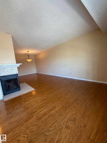 Spacious interior featuring wood-finish flooring, a fireplace with a stone mantel, a tiled hearth, an overhead light fixture, and neutral-toned walls - 2324 151 Avenue Nw, Edmonton, AB - Indoor Photo Showing Other Room