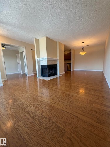 Expansive living area featuring wood-finish flooring, a central fireplace with a stone mantel, recessed lighting, and a dining area chandelier - 2324 151 Avenue Nw, Edmonton, AB - Indoor Photo Showing Other Room With Fireplace