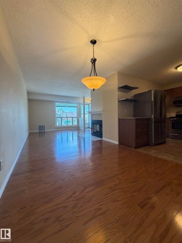 Open-concept living area featuring wood-finish flooring, a contemporary ceiling light fixture, and a fireplace with a stone surround - 2324 151 Avenue Nw, Edmonton, AB - Indoor Photo Showing Other Room