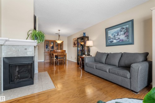 Living area featuring a fireplace with a light-toned stone surround, wood-finish flooring, and a dining space - 2324 151 Avenue Nw, Edmonton, AB 