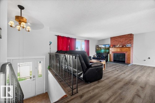 Spacious living area featuring wood-finish flooring, a brick fireplace with a wood mantle, and a large window providing ample natural light - 5215 50 Avenue, Bruderheim, AB - Indoor Photo Showing Living Room With Fireplace