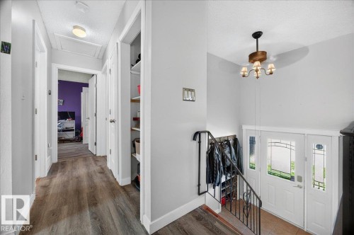 Foyer featuring a decorative chandelier and a staircase with wrought iron railings, leading to a hallway with wood-finish flooring, recessed lighting, and a built-in linen closet - 5215 50 Avenue, Bruderheim, AB - Indoor Photo Showing Other Room