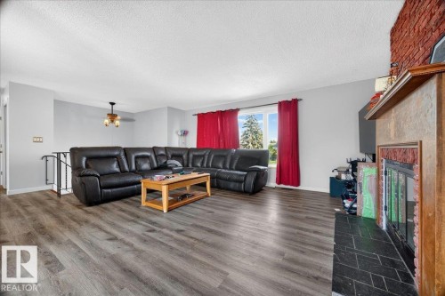 Spacious living area featuring wood-finish flooring, a contemporary fireplace with a stone surround, and an exposed brick accent wall - 5215 50 Avenue, Bruderheim, AB - Indoor Photo Showing Living Room