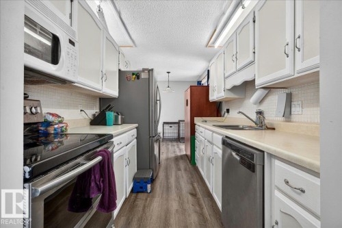 Galley kitchen featuring wood-finish flooring, white cabinetry with silver hardware, a built-in microwave, a stainless steel electric range, and a stainless steel dishwasher - 5215 50 Avenue, Bruderheim, AB - Indoor Photo Showing Kitchen